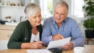 Senior couple sitting at a table reviewing and pointing at documents together in a bright, modern kitchen.
